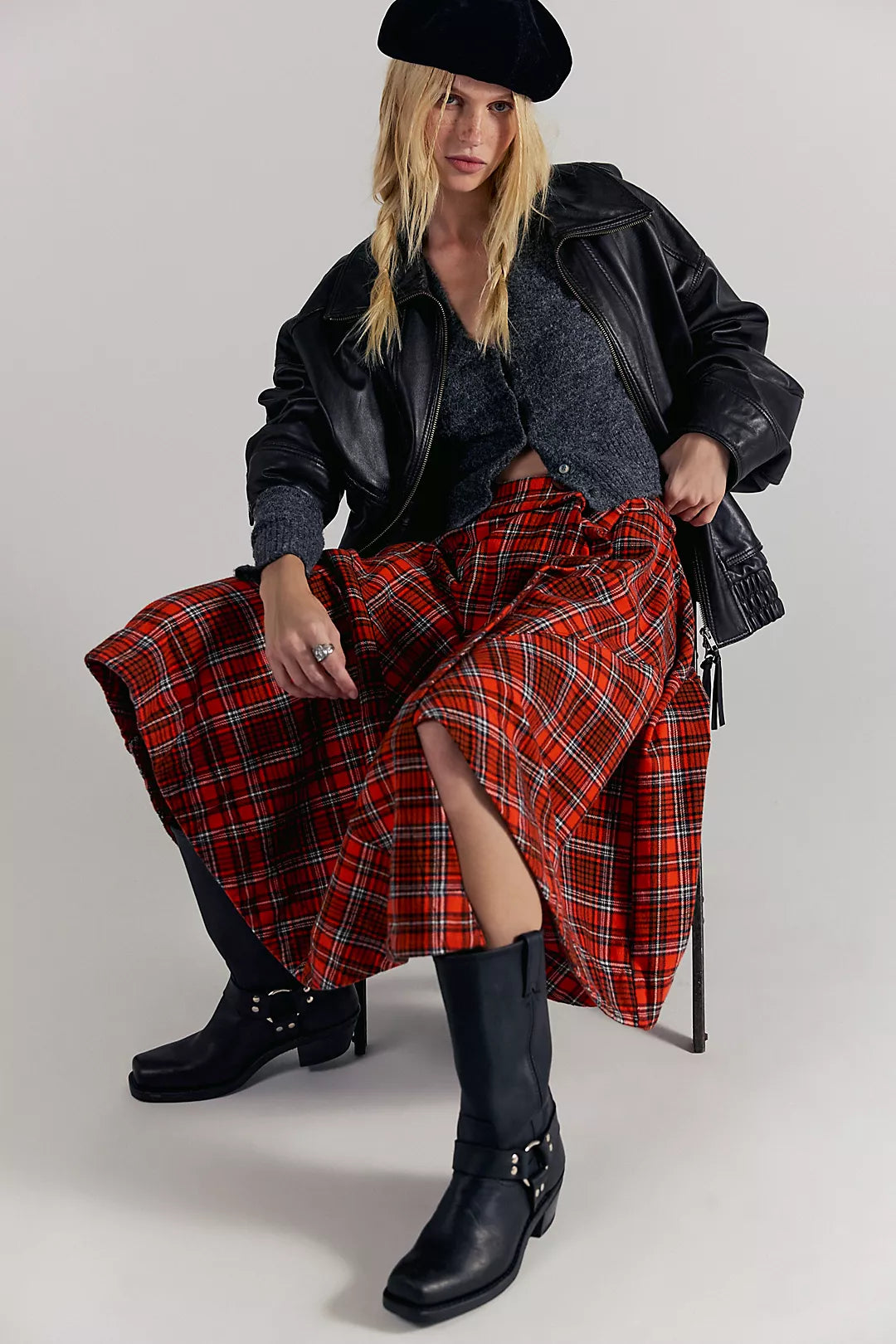 Person wearing a Free People  red plaid skirt, black jacket, and black boots on a white background