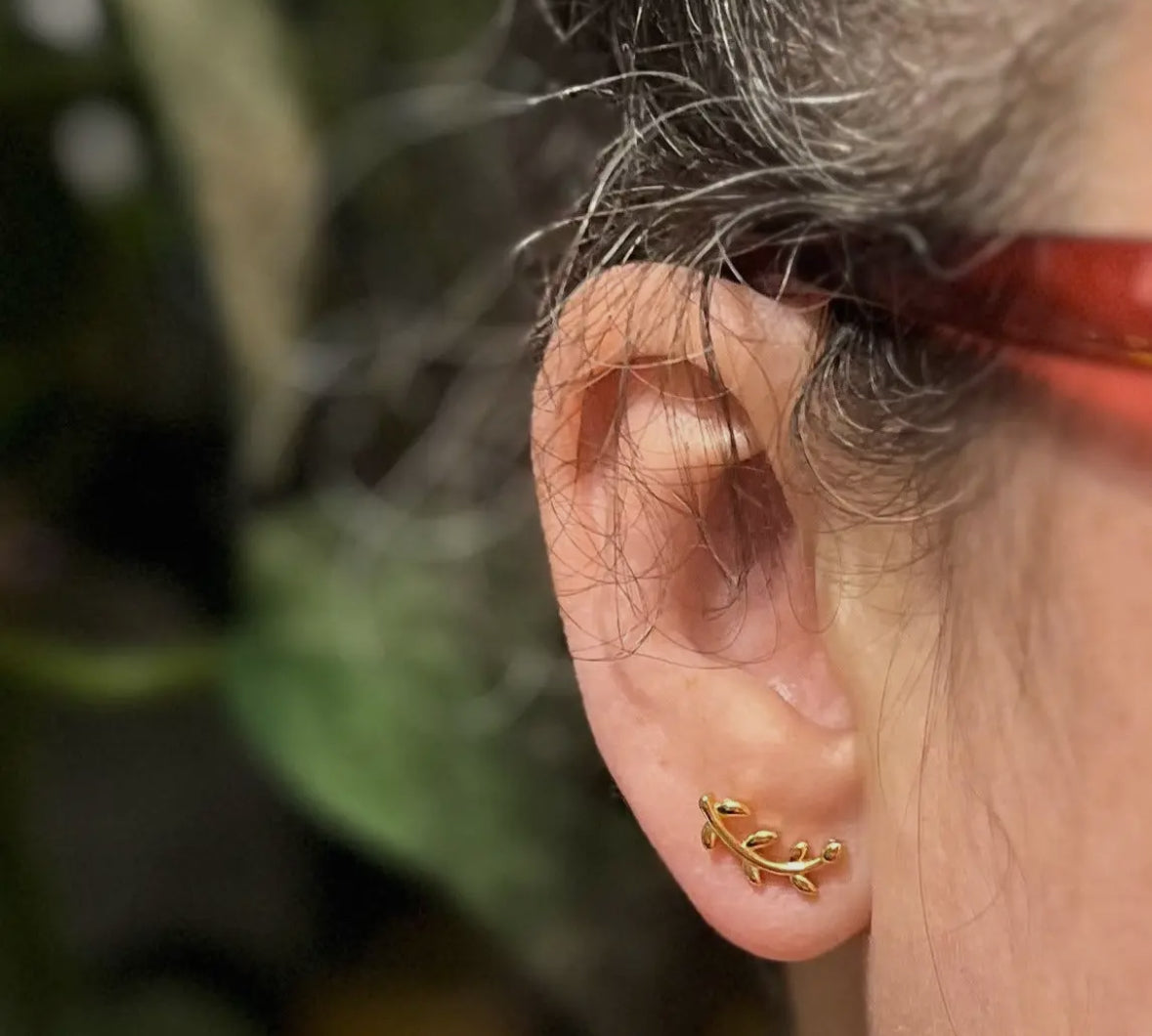 Close-up of an ear wearing a gold earring with a blurred natural background