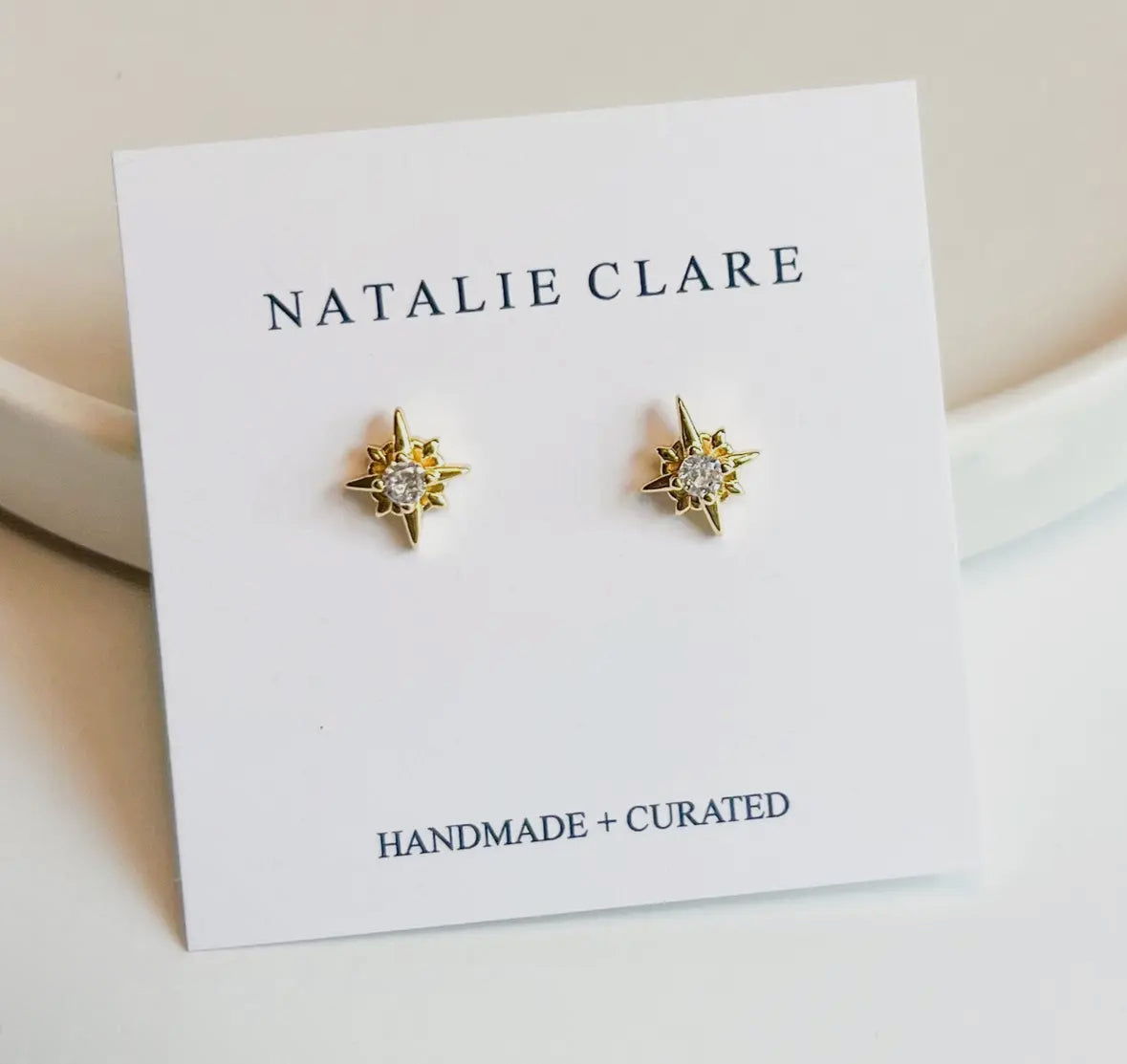 Gold star-shaped earrings on a 'Natalie Clare' branded card.