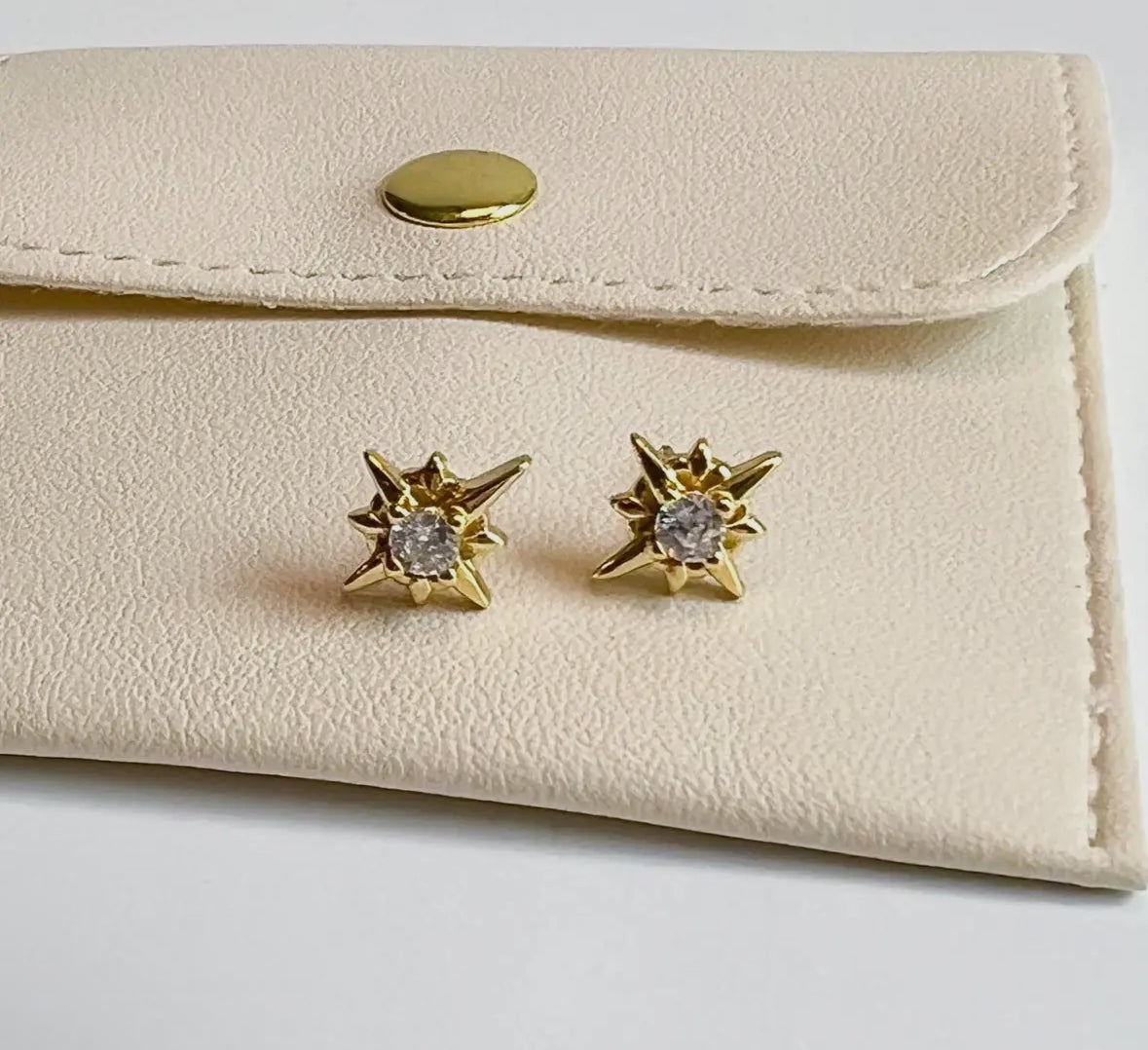 Gold star-shaped earrings with clear stones on a beige jewelry pouch.