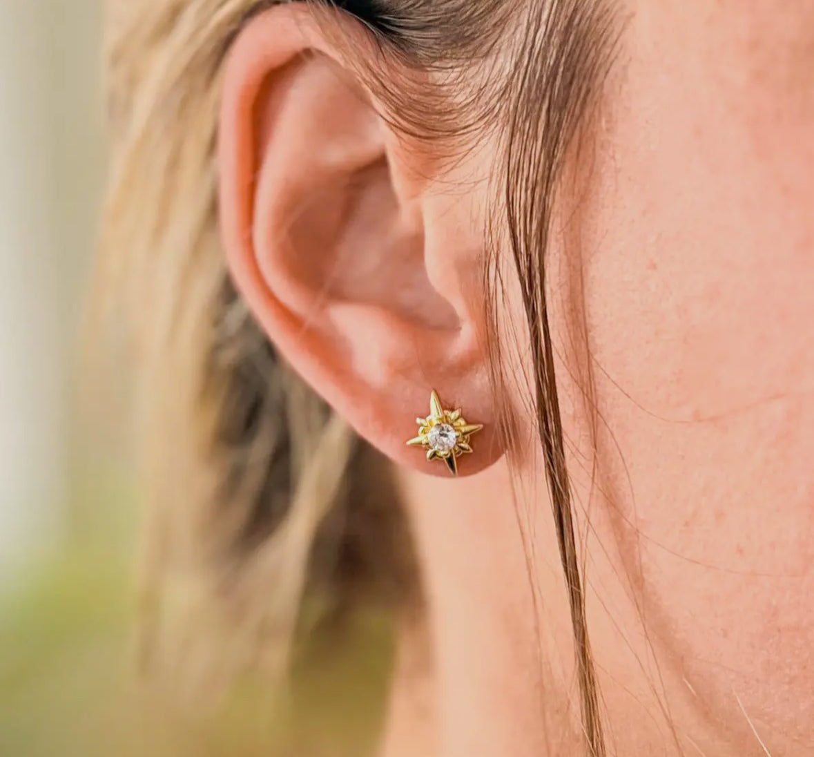 Close-up of an ear wearing a star-shaped gold earring with a clear gemstone.