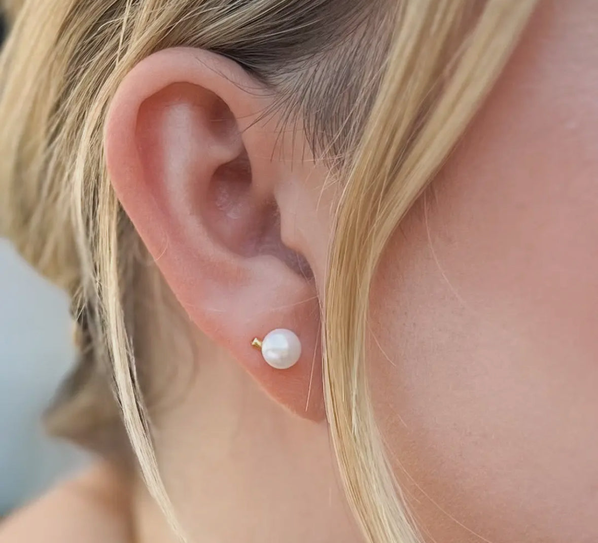 Close-up of an ear wearing a pearl earring with blonde hair.