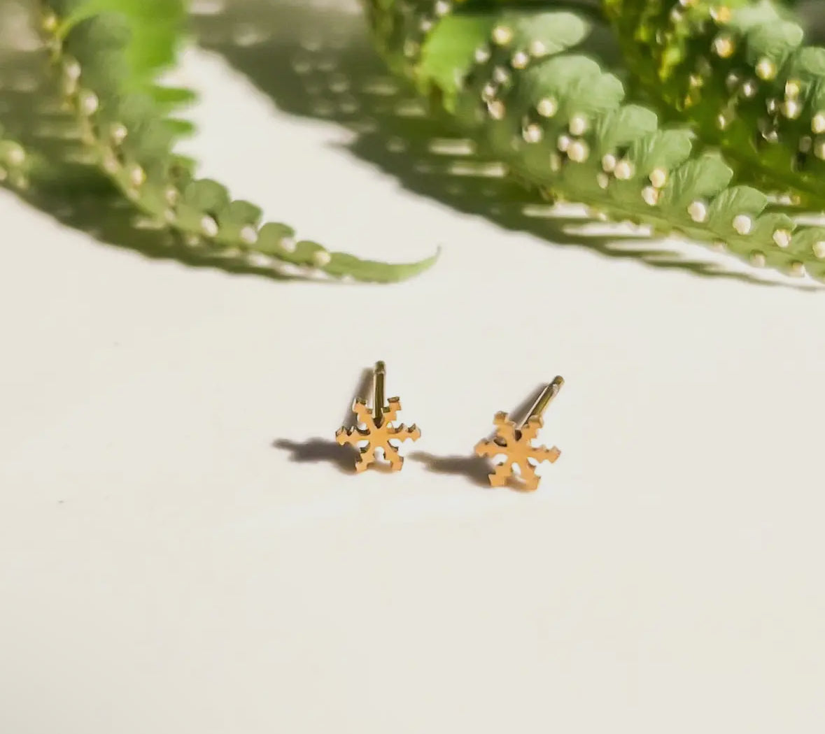 Gold snowflake earrings on a light surface with green leaves in the background