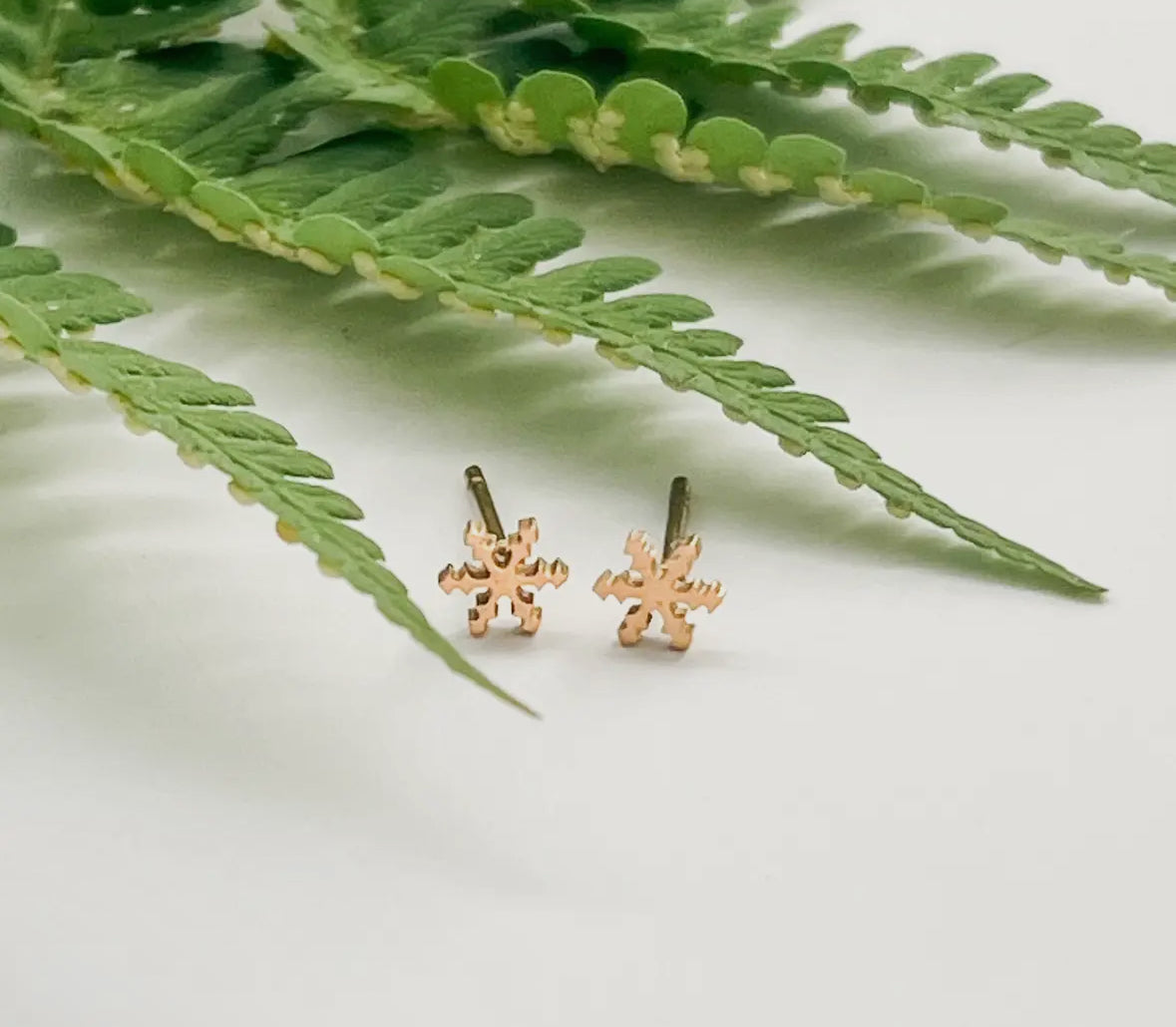 Gold snowflake earrings on a white surface with green leaves