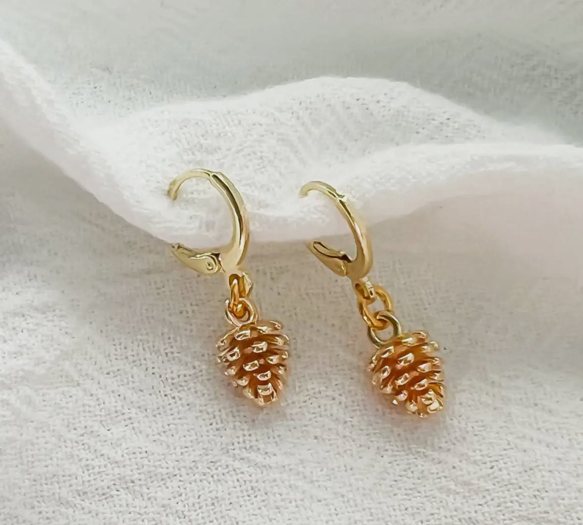 Gold pinecone-shaped earrings on a white fabric background