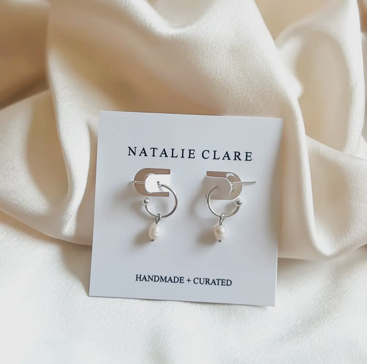 Pair of earrings on a 'Natalie Clare' branded card with a soft beige background