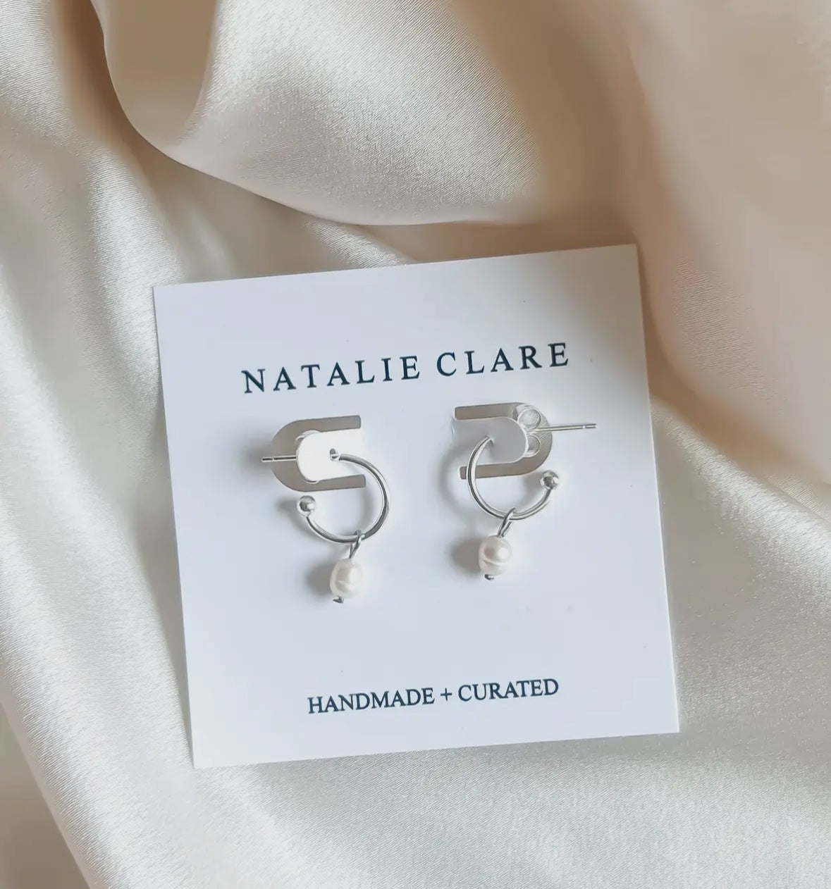 Silver earrings with pearls on a 'Natalie Clare' branded card against a soft beige background