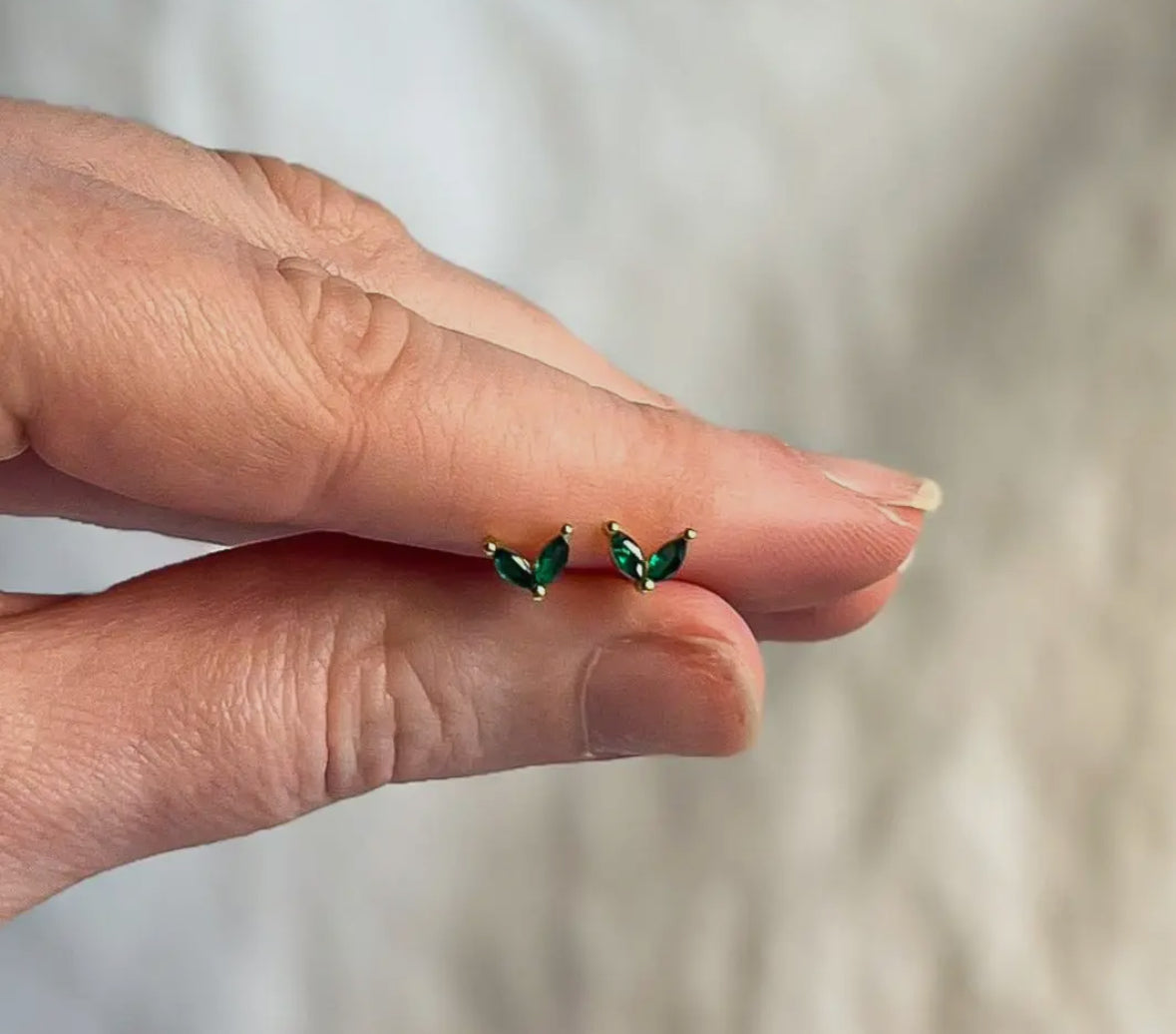 Hand holding a pair of green earrings against a neutral background