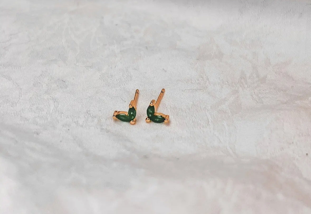 Pair of gold earrings with green gemstones on a white fabric background