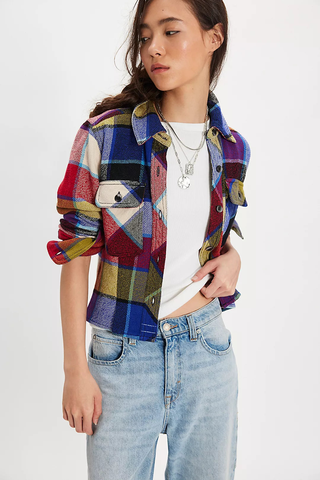Person wearing a Free People colorful patchwork jacket and light blue jeans on a white background