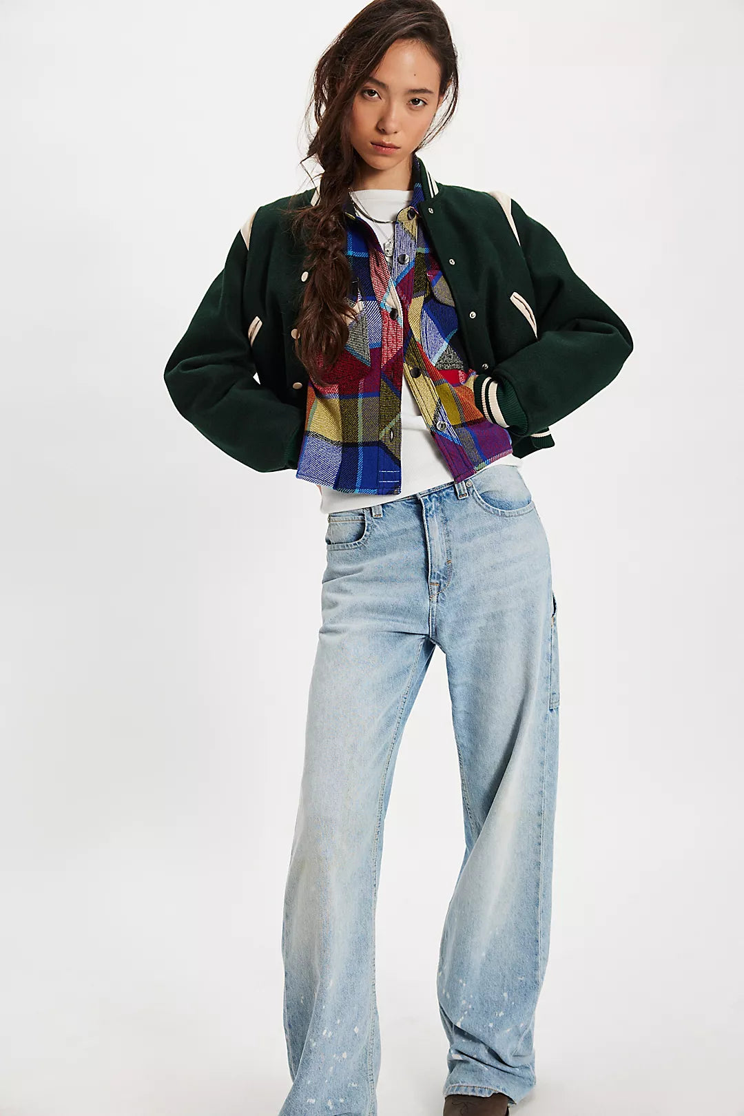 Person wearing a dark green jacket, Free People colorful plaid shirt, and light blue jeans on a white background