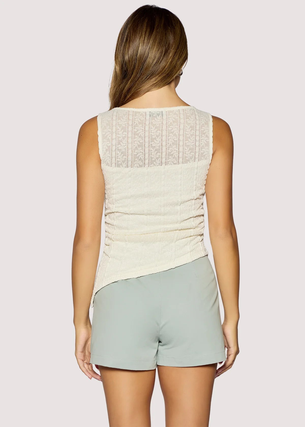 Woman wearing a cream sleeveless top and light gray shorts on a plain background