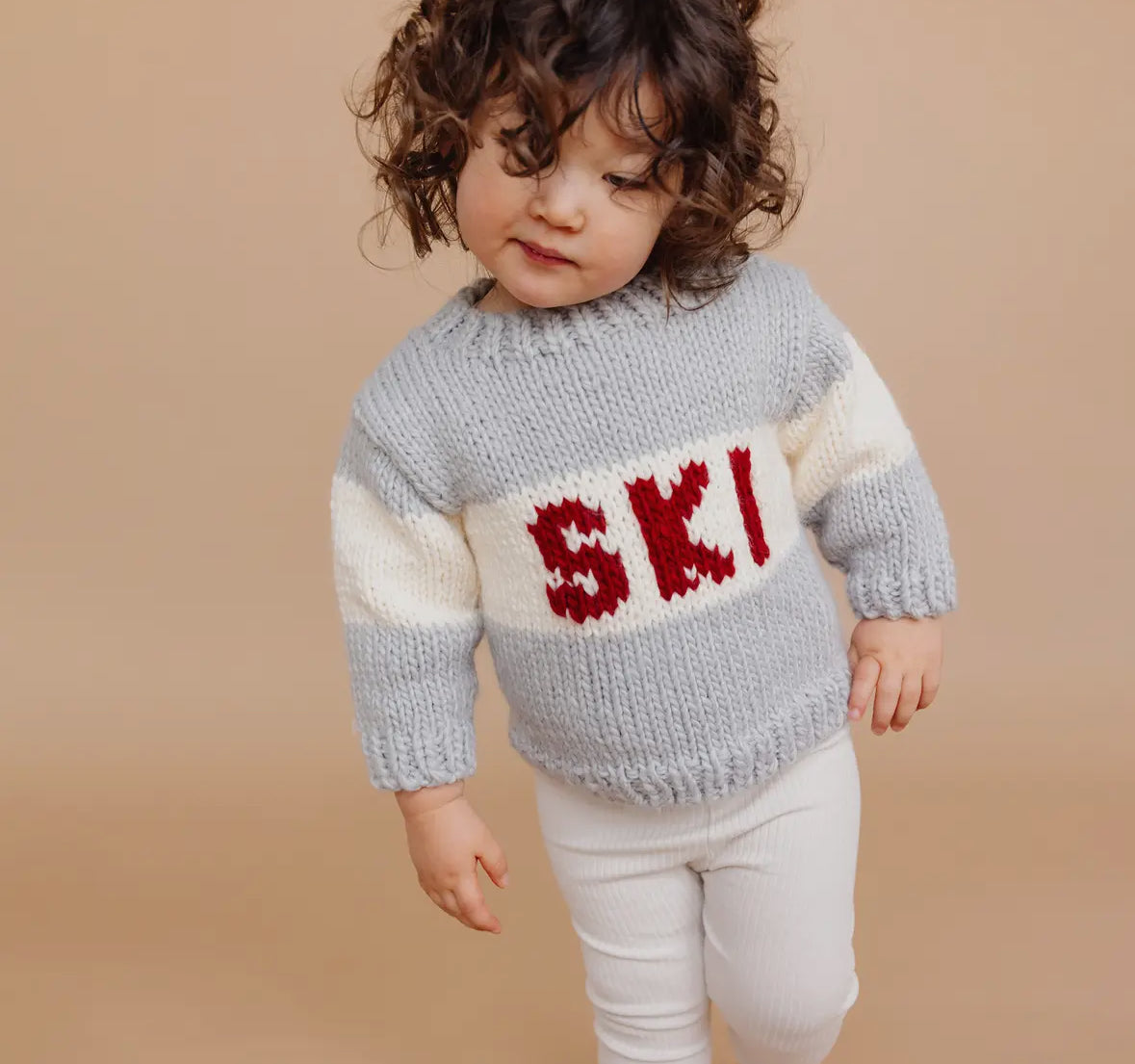 Child wearing a gray sweater  from Blueberry Hill with 'SKI' in red and white on a beige background, 