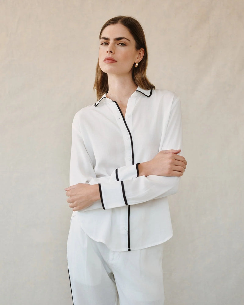 Woman wearing a white outfit with black trim against a plain background