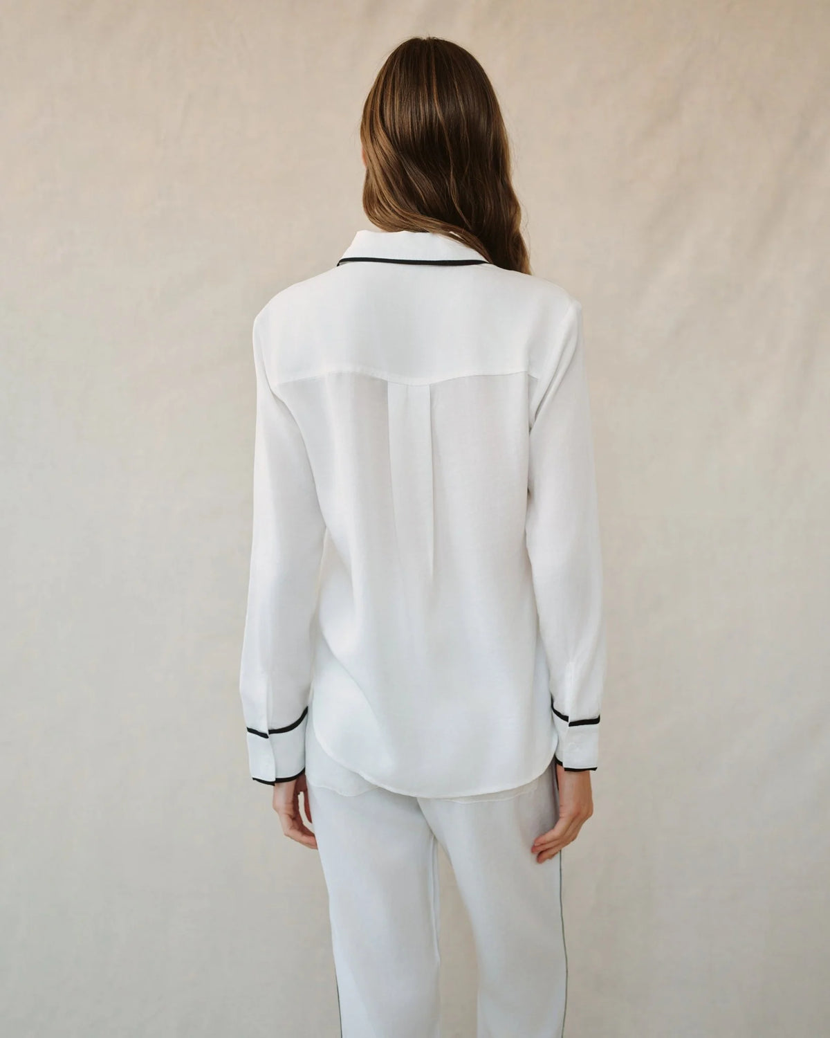Person wearing a white shirt with black trim on a plain background