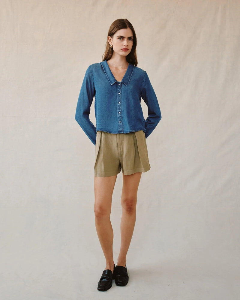 Woman wearing a blue shirt and beige shorts against a plain background