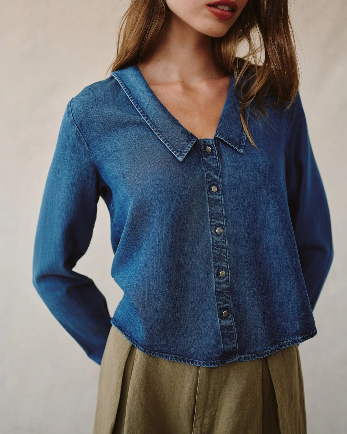 Blue denim shirt worn by a person on a neutral background