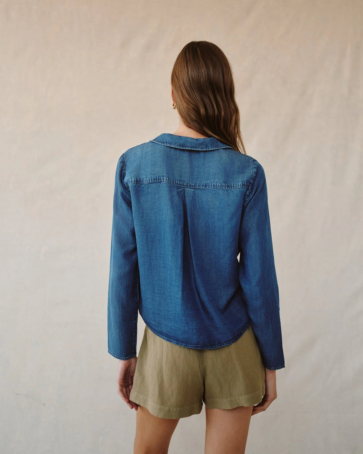 Person wearing a blue denim shirt and beige shorts against a plain background