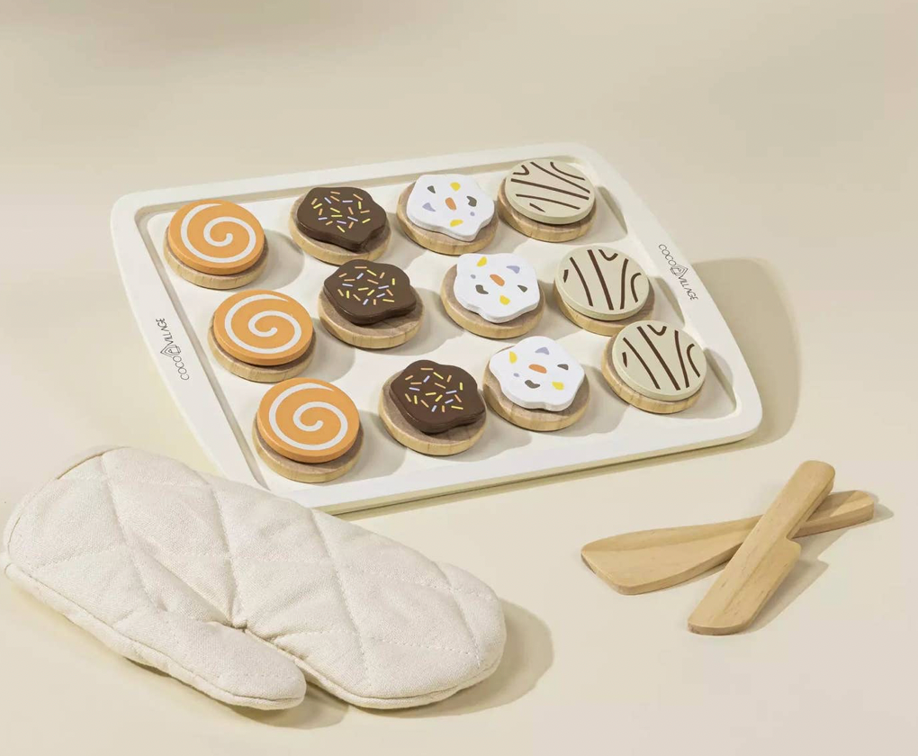 Set of wooden cookies with icing, a tray, oven mitts, and spatulas on a beige background