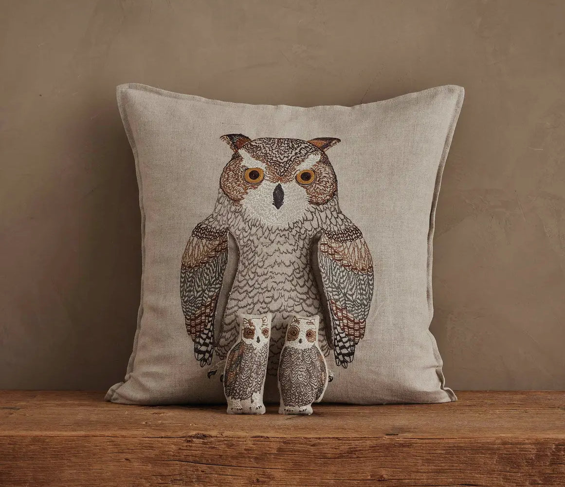 Decorative pillow with an owl design on a wooden surface against a beige background