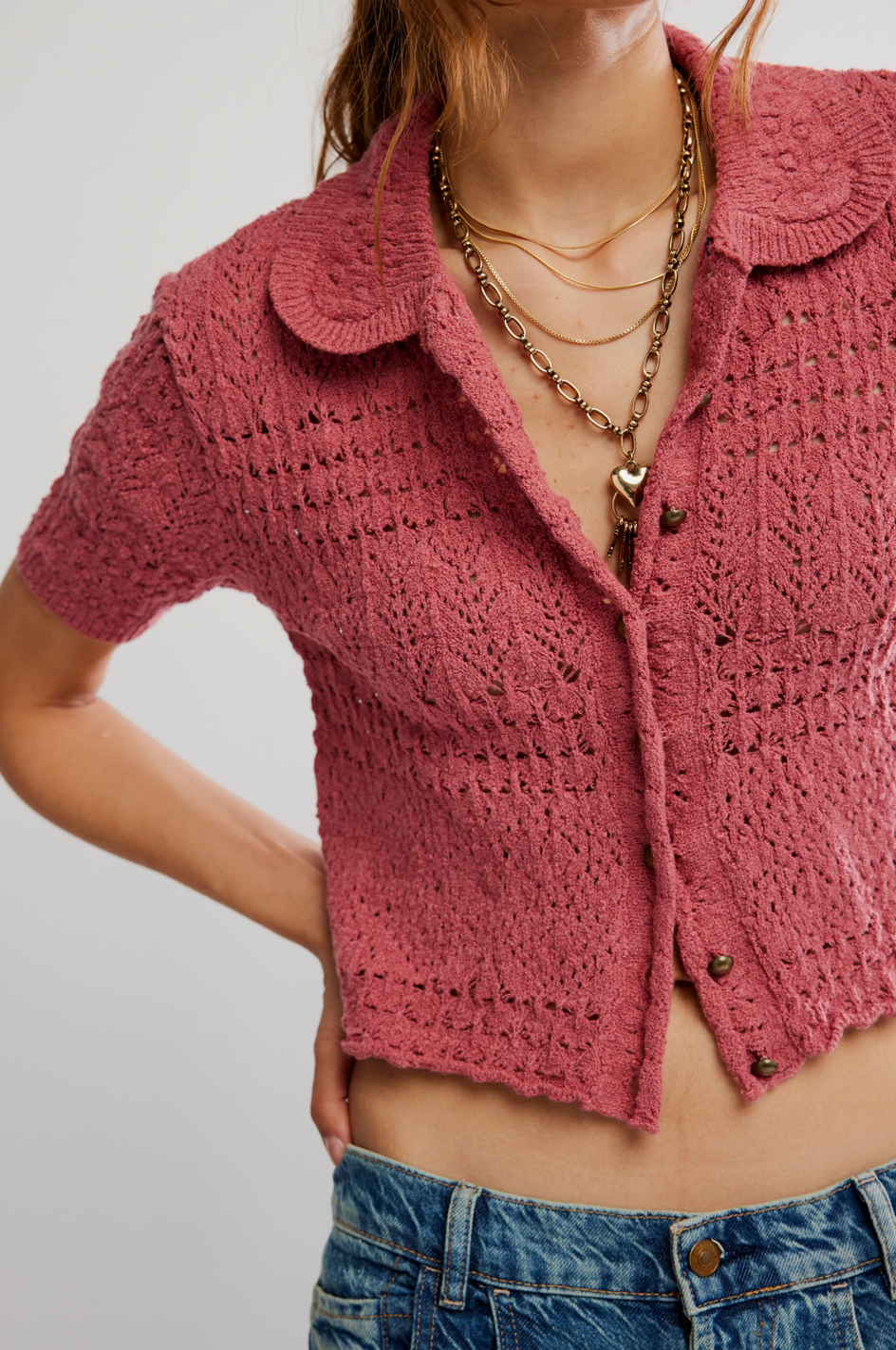 Person wearing a pink knitted cardigan over a blue denim outfit on a plain background