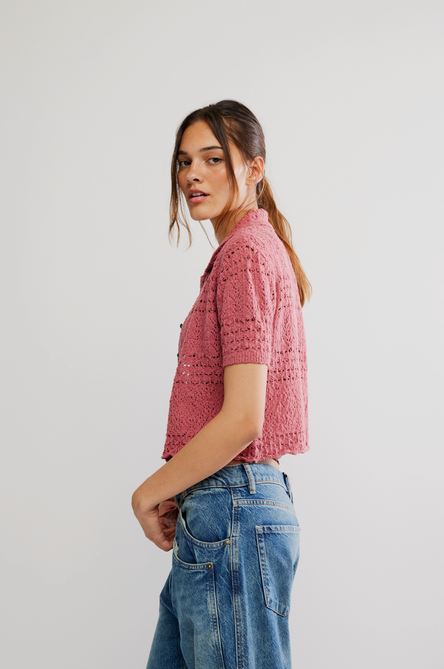 Woman wearing a pink textured shirt and blue jeans on a white background