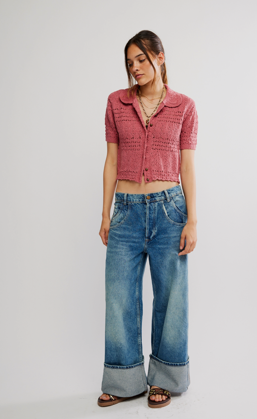 Woman wearing a pink knitted cardigan and blue jeans on a white background
