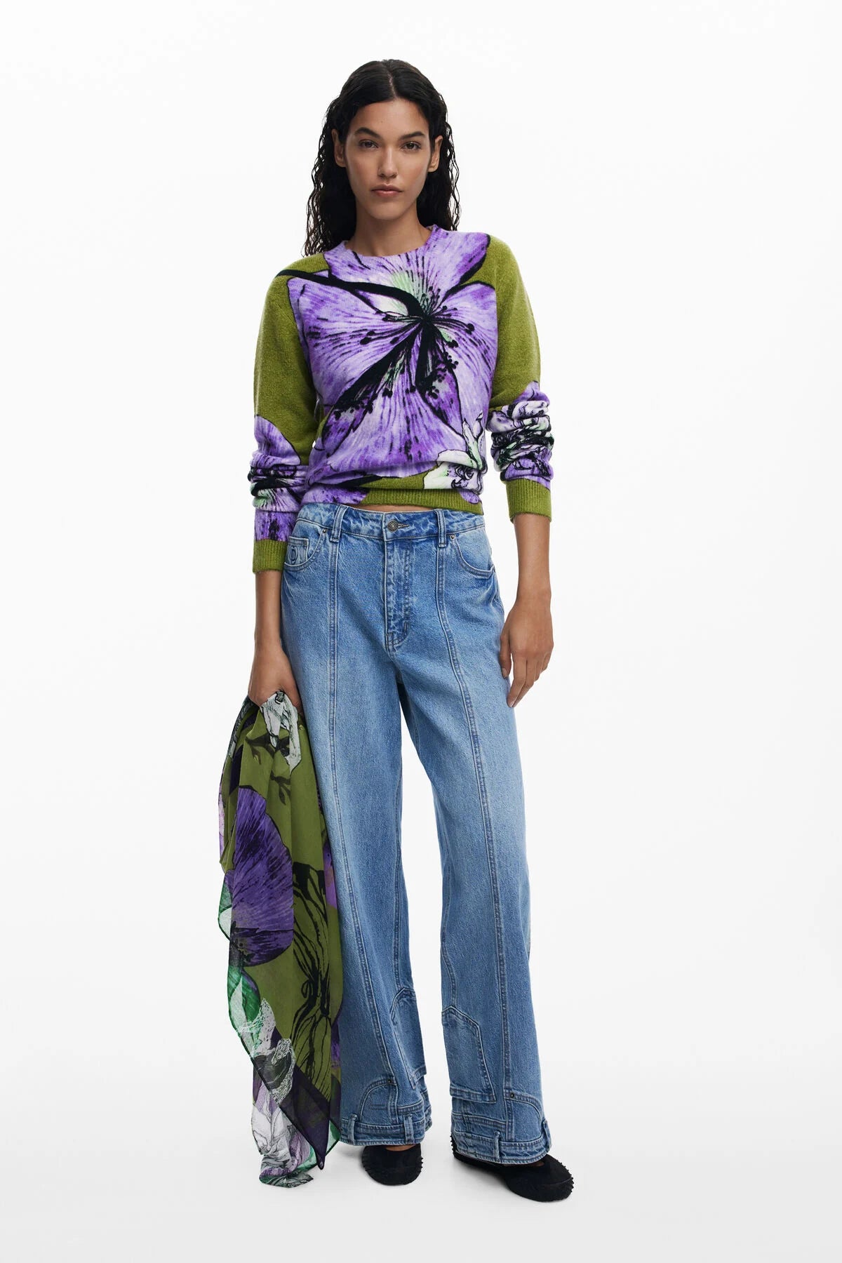 Model wearing a colorful top and jeans with a white background