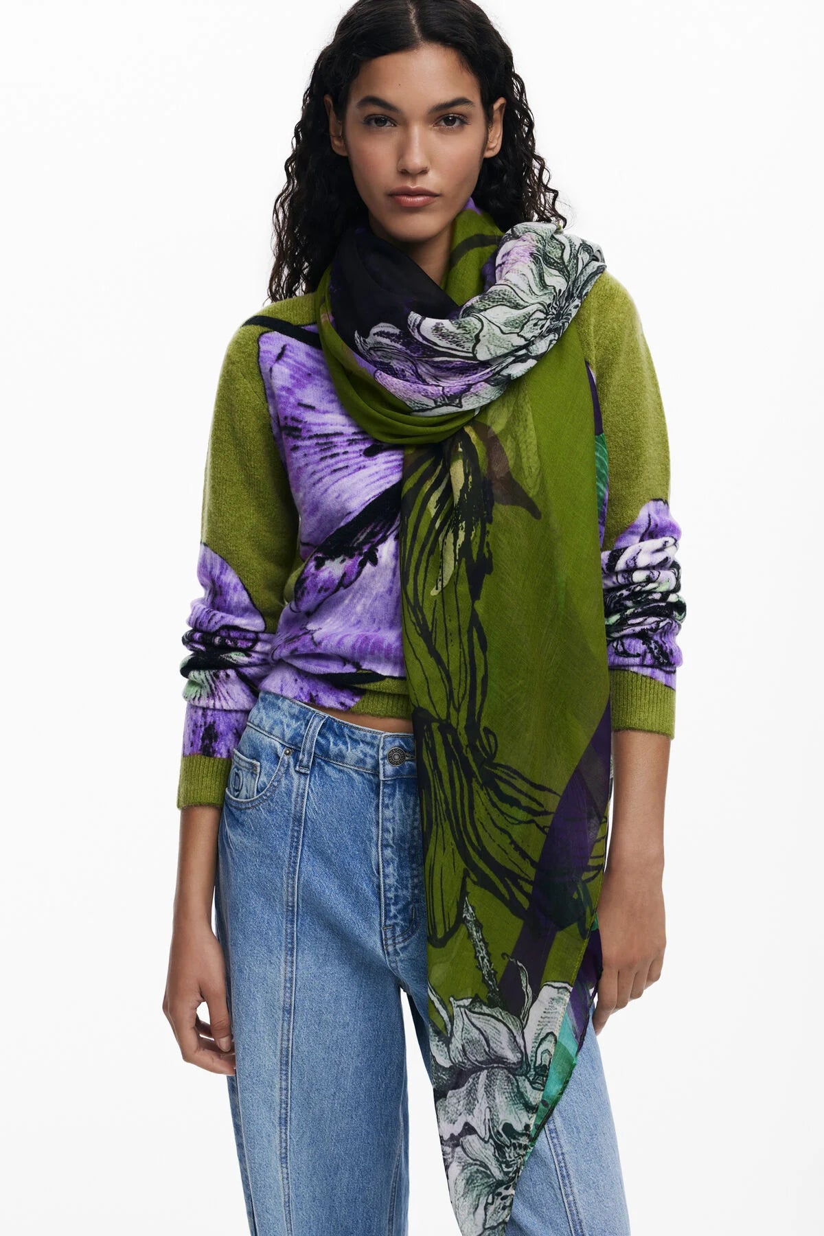 Woman wearing a green sweater with a floral scarf, standing against a white background