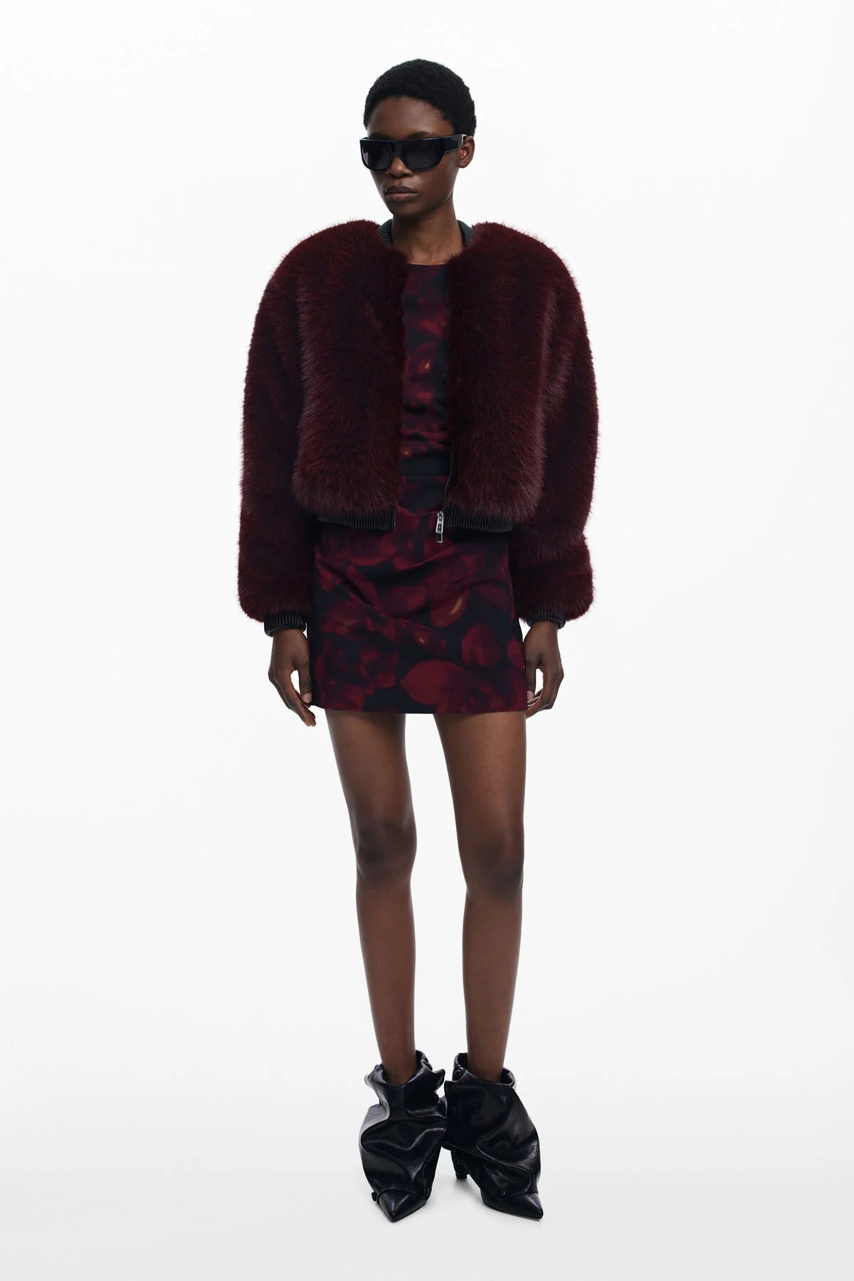 Person wearing a burgundy fur coat, dress, and shoes on a white background