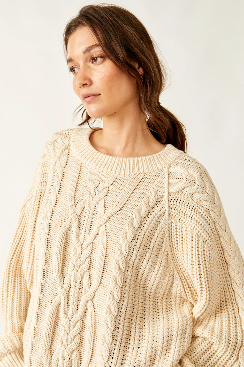 Woman wearing a beige cable knit sweater against a white background
