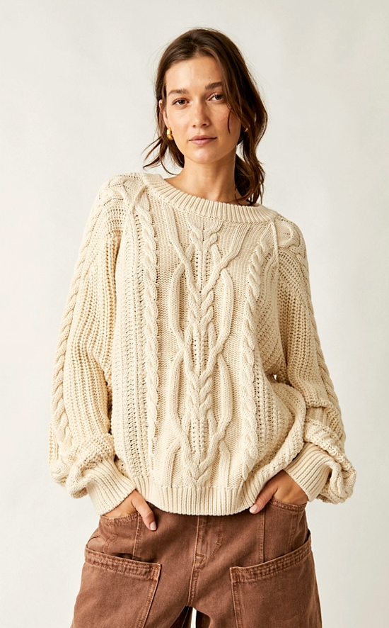 Woman wearing a beige cable knit sweater against a white background