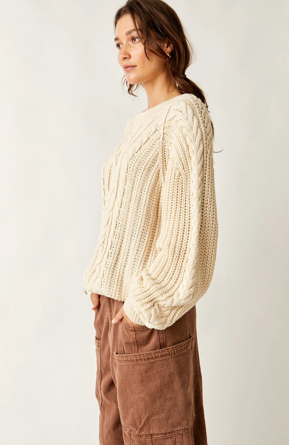 Woman wearing a cream knitted sweater and brown pants against a white background