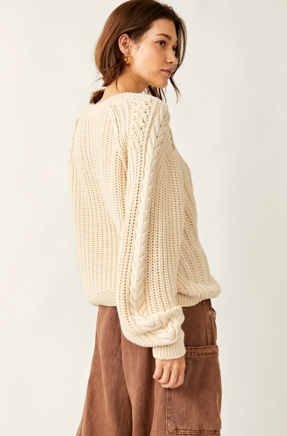 Woman wearing a cream chunky knit sweater and brown pants on a white background