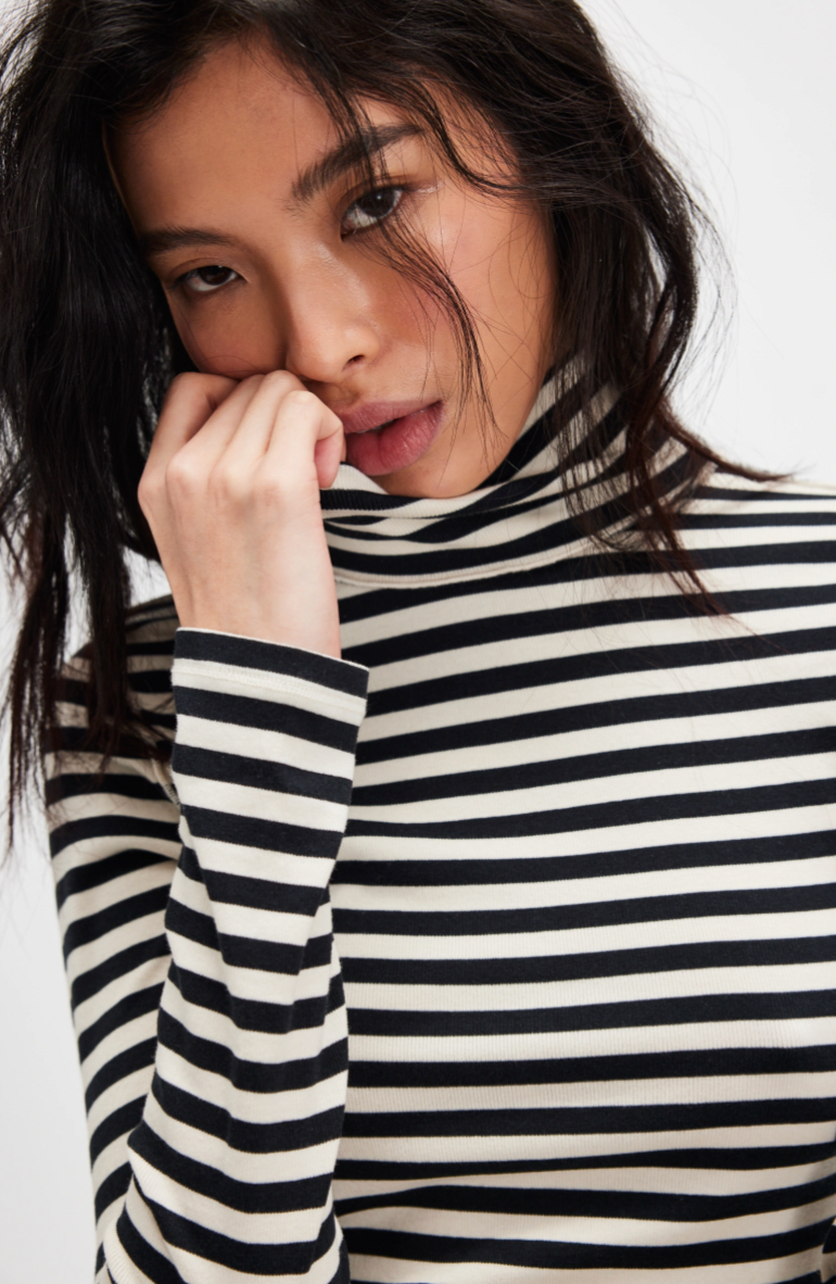 Woman wearing a black and white striped turtleneck sweater against a white background