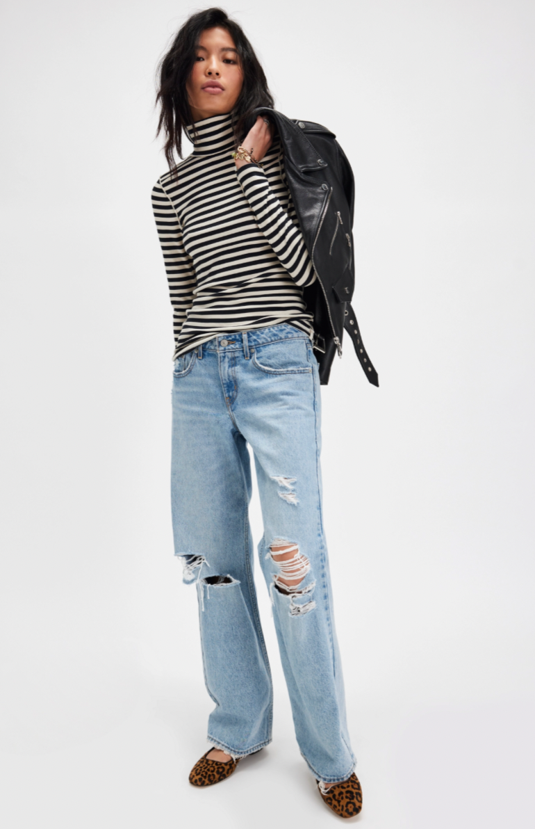 Person wearing a striped turtleneck, leather jacket, and ripped jeans on a white background