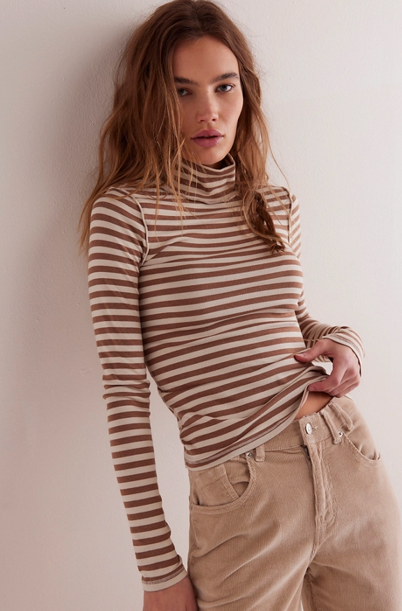 Woman wearing a striped turtleneck and beige pants against a plain background