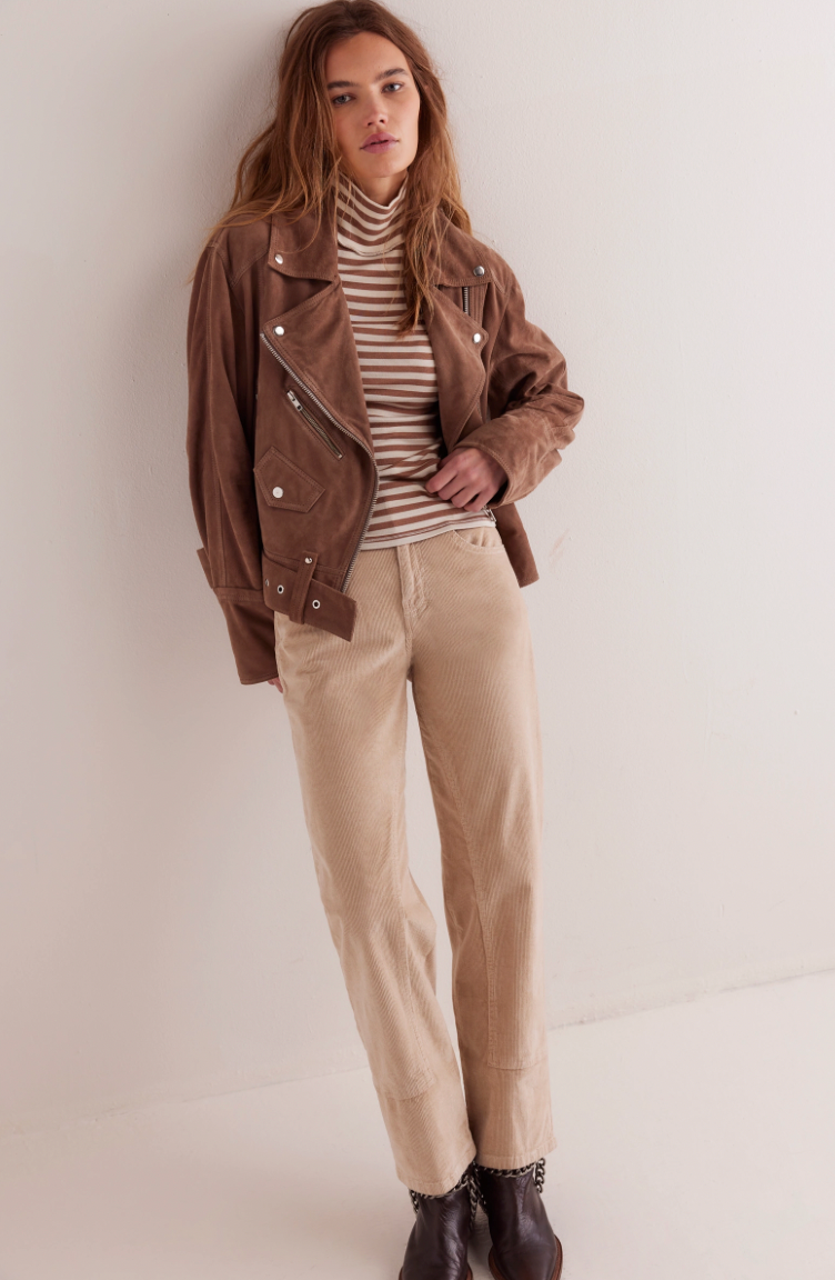 Woman wearing a brown jacket, striped sweater, beige pants, and black boots against a white background