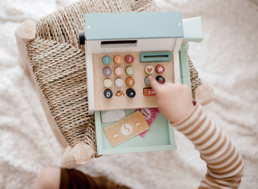 Child's hand interacting with a toy cash register on a soft surface