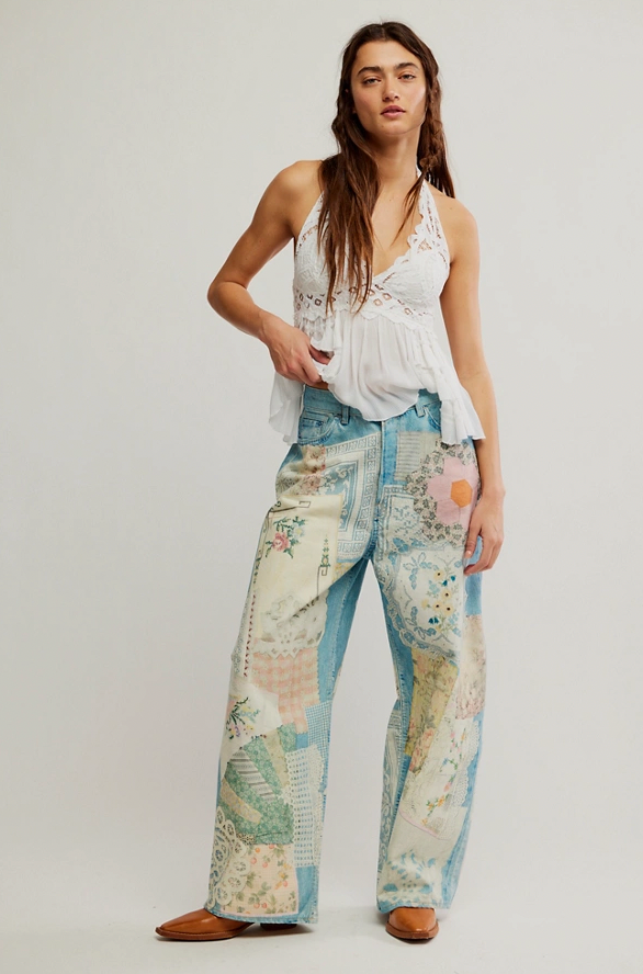 Woman wearing a white sleeveless top and patterned pants on a plain background