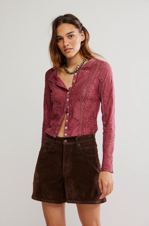 Woman wearing a pink lace top and brown shorts on a plain background