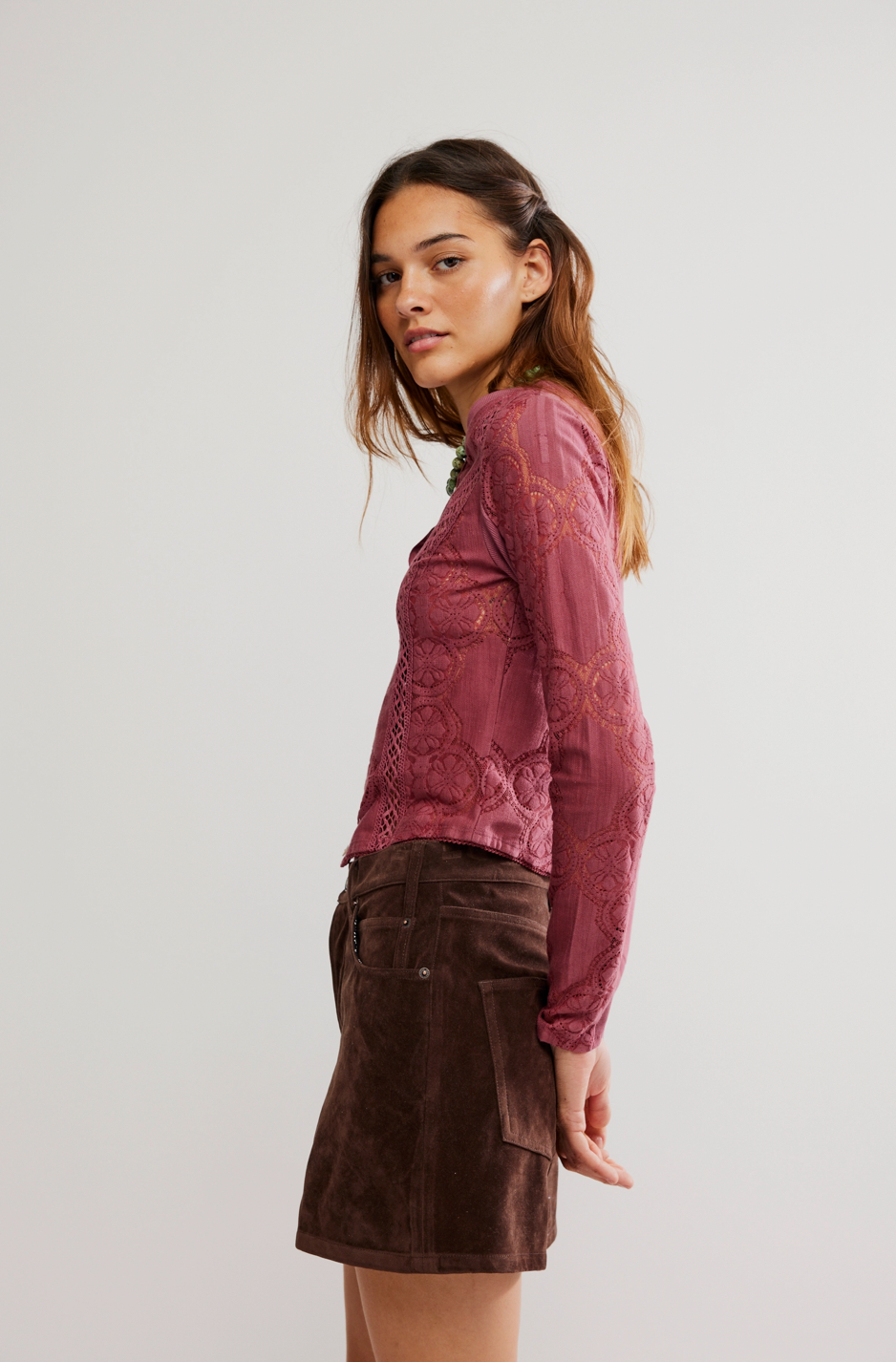 Woman wearing a pink lace top and brown skirt on a white background