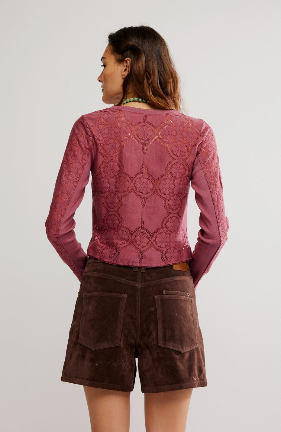Person wearing a pink lace top and brown shorts on a plain background