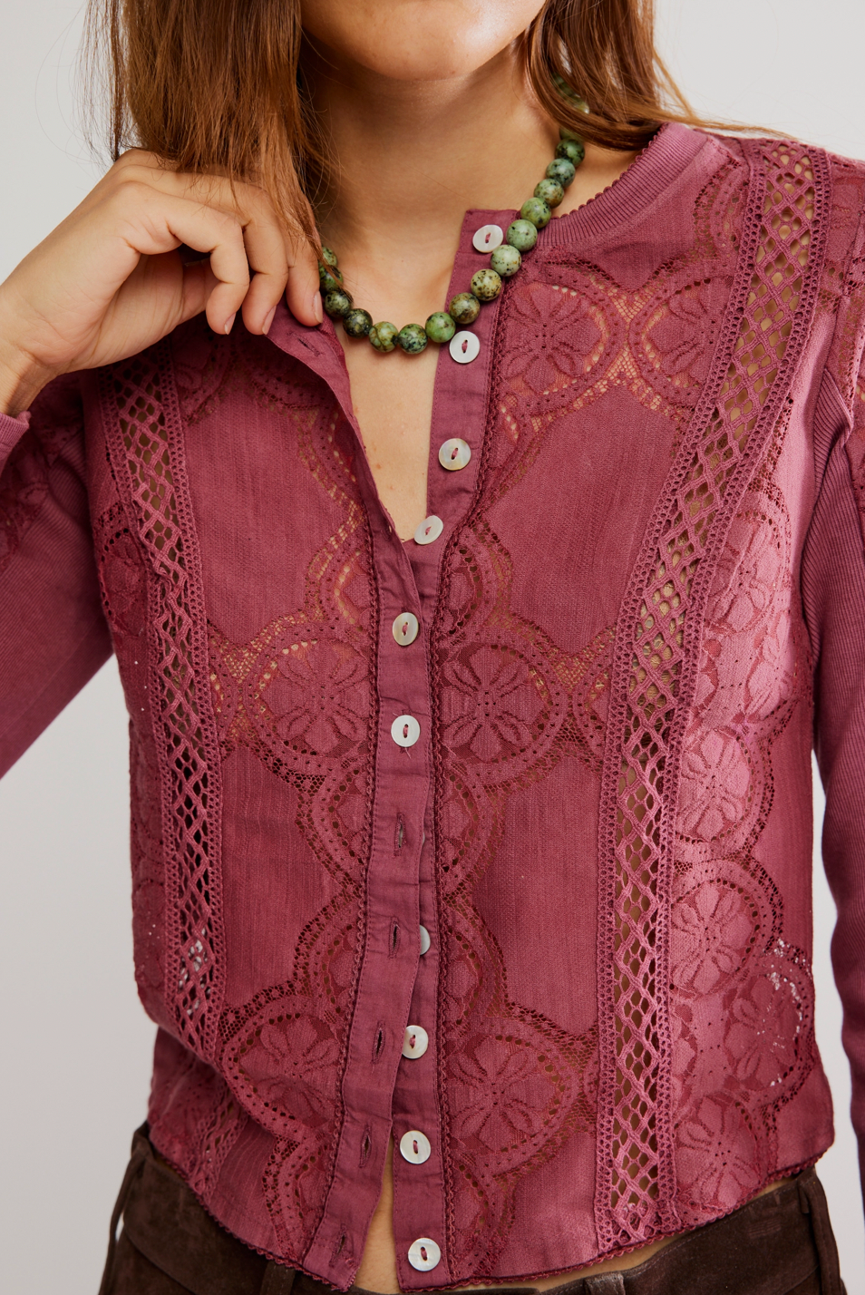 Close-up of a person wearing a burgundy lace shirt with a green necklace.