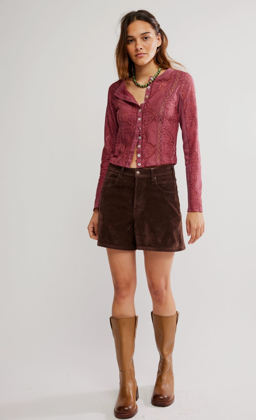 Woman wearing a red patterned shirt, brown shorts, and brown boots on a white background
