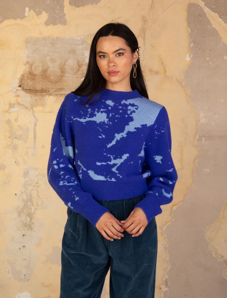 Woman wearing a blue patterned sweater against a textured beige wall