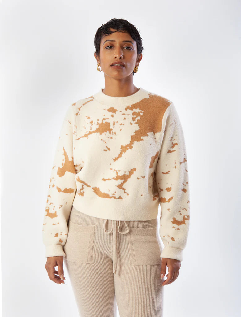 Person wearing a cream and brown tie-dye sweater with beige pants on a white background