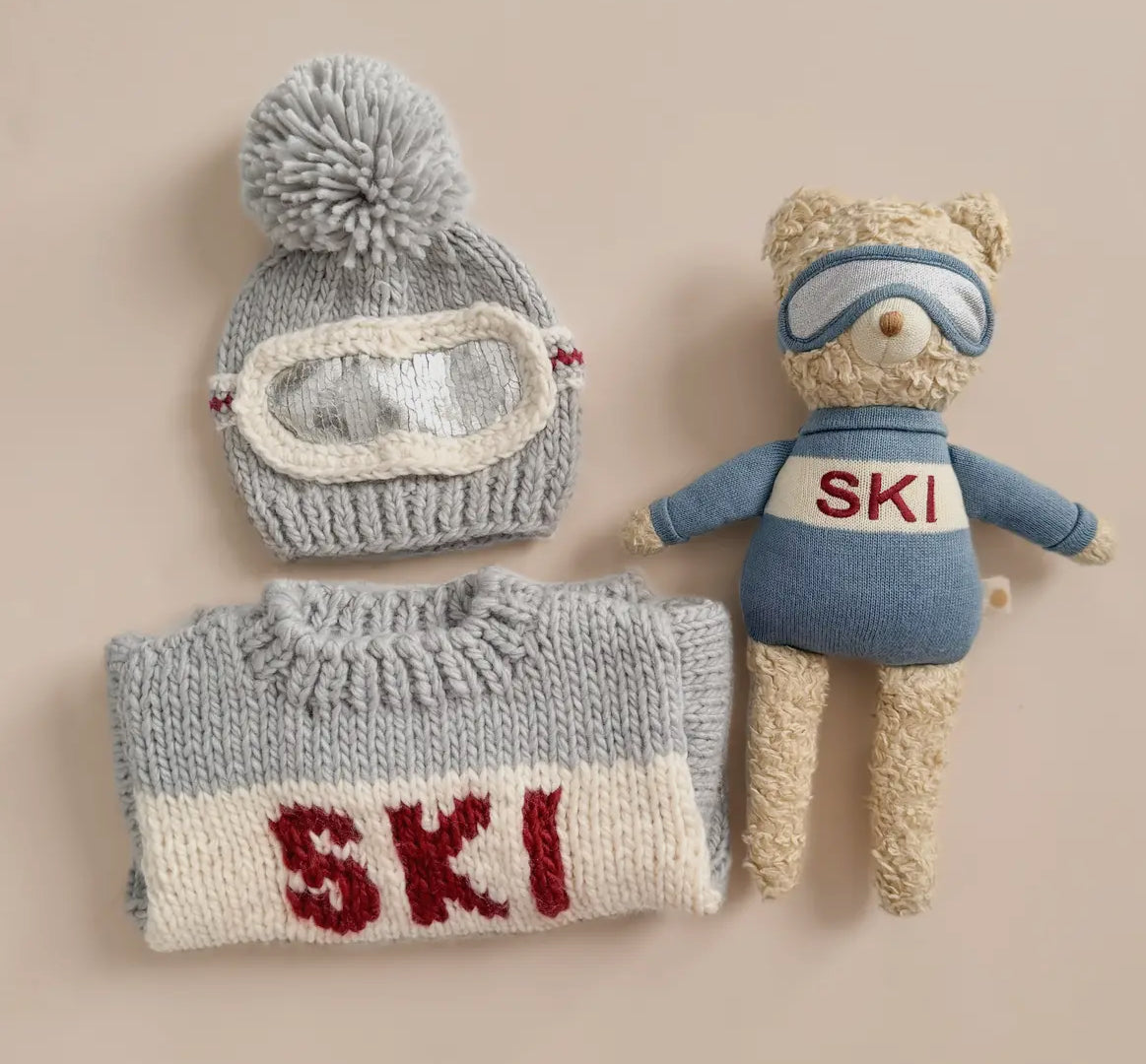 Knitted ski sweater from Blueberry Hill with hat, scarf, and teddy bear on a beige background.