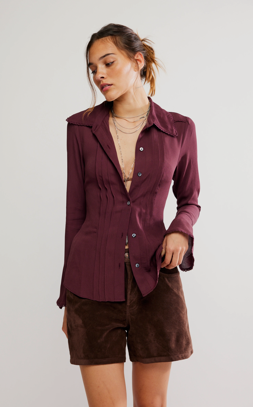 Woman wearing a burgundy button-up shirt and brown shorts on a plain background