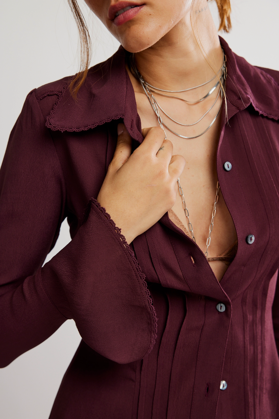Close-up of a person wearing a burgundy shirt with buttons, layered necklaces, and a blurred background.